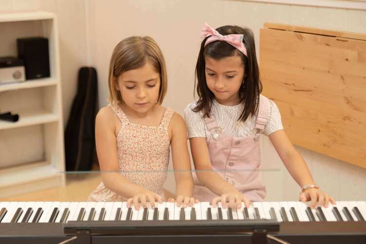 Niñas de 5 años aprendiendo a tocar el piano en clase de música.